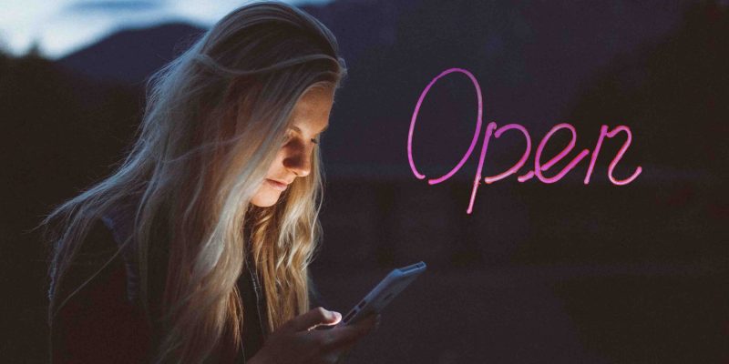 woman on phone at nigh Benefits of a Call Center t with light shining into her face and a pink open sign glowing in the dark